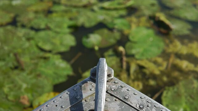 
Old boat metal nose close-up view sailing by the river with refocus to a water lily thickets
