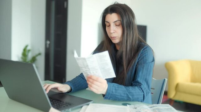 Woman stressed while paying bills online with receipts scattered on table