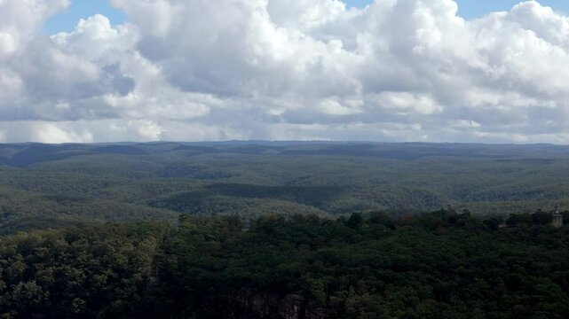 An expansive view of rolling hills or mountains densely covered in dark green forests, extending to the horizon under a dramatic sky with puffy clouds in New South Wales, Australia