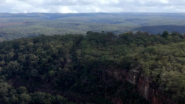 An expansive view of rolling hills or mountains densely covered in dark green forests, extending to the horizon under a dramatic sky with puffy clouds in New South Wales, Australia
