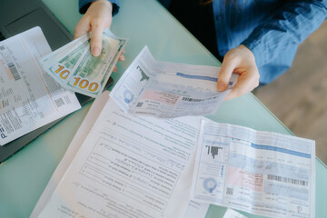 Naklejka premium Hands Holding Cash and Utility Bills on Desk with Laptop in Background