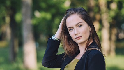 Naklejka premium Professional businesswoman smoothing hair outdoors, embodying corporate confidence and polished demeanor