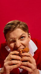 Close-up portrait of handsome young man with one eye closed biting delicious burger with intense...