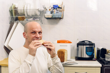 Young man chewing mouth and enjoying tasty fresh bread baked by himself. Bald man chewing bread in...