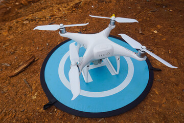 White quadcopter drone on a blue landing pad set on dry soil, ready for takeoff. Aerial photography...