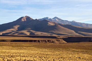 Naklejka premium Close-up view of volcanic mountain range in Eduardo Avaroa National Reserve, Bolivia. Distinctive multi-peaked formation with light and shadow playing on slopes. Golden grassland foreground.