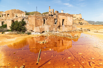 Abandoned mining ruins and cracked orange toxic pond in Mazarrón, Murcia, Spain, reflecting industrial decay, environmental contamination, and surreal desert transformation under harsh sunlight