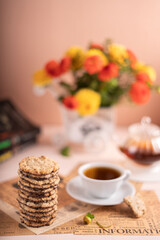 photo A delightful tea time scene showcasing a stack of delicious cookies on newspaper alongside a cup of tea and vibrant flowers in a vase for a cozy afternoon relaxation