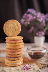 photo Delicious Stack of Cream-Filled, Crispy Cookies with Aroma of Fresh Floral Accents and Aromatic Drink in Perfect Harmony on Rustic Paper Setting