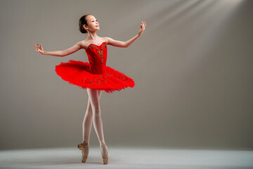 Young Japanese ballerina in red tutu and pointe shoes dances classical dance on light background.