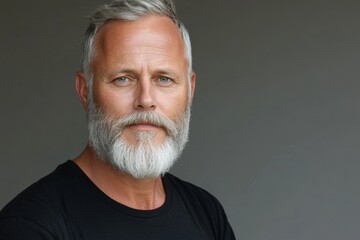 Fototapeta premium Man with gray beard poses confidently against a neutral background in a relaxed atmosphere, showcasing an engaging expression