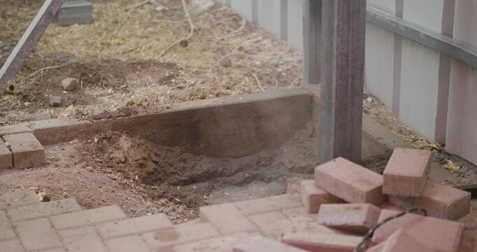 Person using shovel to fill the the base around a timber post that has been concreted into the gorund