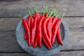 Fresh red chili peppers arranged on a rustic stone plate over a wooden table, showcasing vibrant color and natural texture.