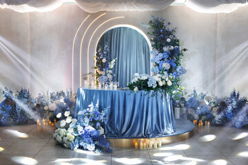 Wedding table for the bride and groom is decorated with a tablecloth, flowers and candles in blue.