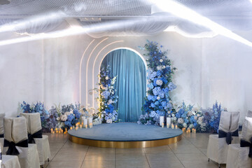 Arch for the wedding ceremony is decorated with blue flowers, spotlights and a podium.