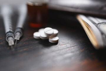 White pills, narcotics or medicine, syringes and glass vial with substance, wallet and US dollar banknotes on a dark wooden table, close-up view