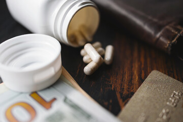 White medicine capsules and medication pills with US dollar banknotes, credit card and wallet, close-up view