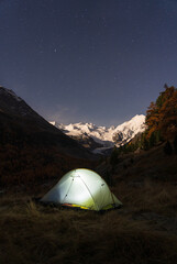 A tent under the night sky in the moonlit Bernina mountain group, Switserland.