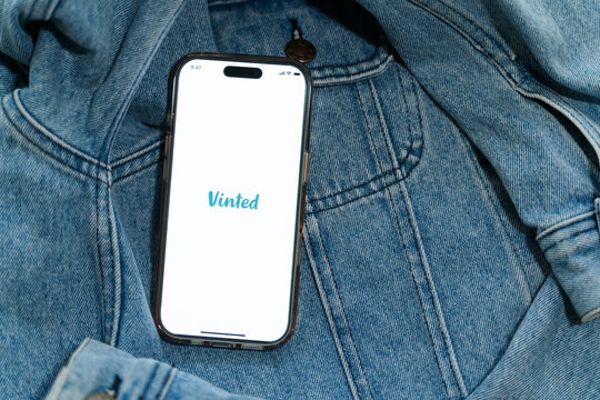 Iphone with vinted logo on screen on vintage denim fabric. Vinted is a Lithuanian online marketplace and community for second hand clothes and accessories.