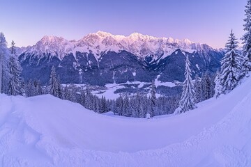Panoramic sunrise view of snow-covered mountain range, valley, and evergreen forest