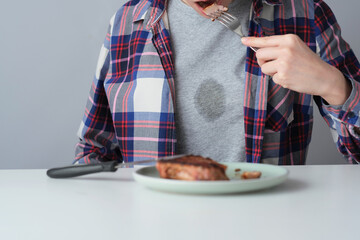 Tough grease stain on clothes. A person siting at a dining table, using a knife and fork to cut...