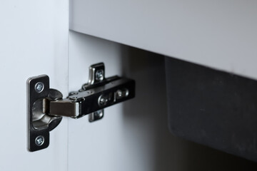 Close-up of kitchen cabinet hinge and accessories with white storage cabinet and sink in the...