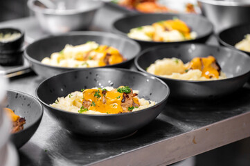 A row of dark bowls filled with creamy mashed potatoes topped with tender meat and melted cheese, elegantly presented, showcasing a mouthwatering meal ready for serving.