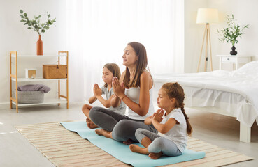 Relaxed family mother and her children sitting on sport mat, doing yoga breathing exercise. Happy...