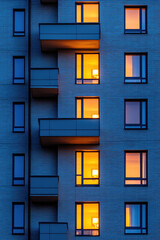 Frontal view of the building's night facade with many illuminated windows. Background of a residential building facade.