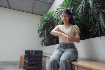 Young woman is sitting on a bench scratching her arm, suffering from strong allergy itching skin rash caused by mosquito bites or insect bites, feeling unwell and uncomfortable © Tj