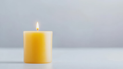 A single burning yellow candle sits peacefully against a muted gray background providing a warm and inviting glow in a calming and serene atmosphere now.