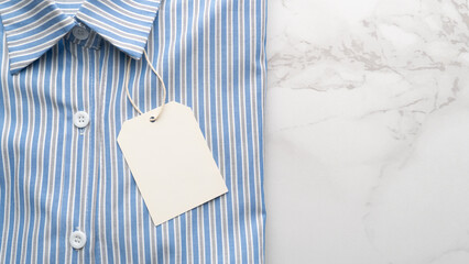 Blue striped shirt with blank tag label on marble background. Mock up for design.