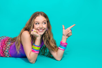 Young woman in vibrant retro attire pointing with a cheerful smile, turquoise background, trendy...