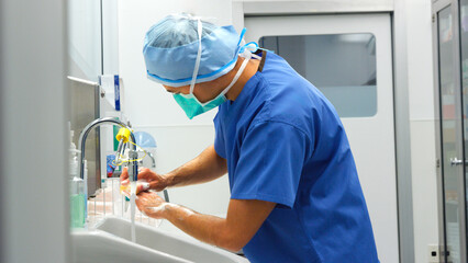Male Surgeon Wearing Scrubs Washing Hands Before Operation In Hospital Operating Theater