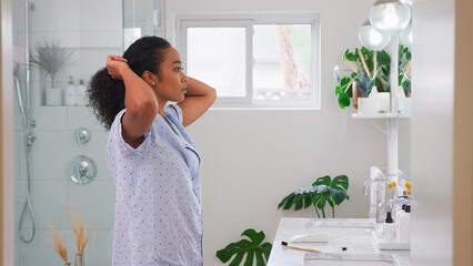 Woman Wearing Pyjamas Standing In Front Of Bathroom Mirror Putting Hair Up