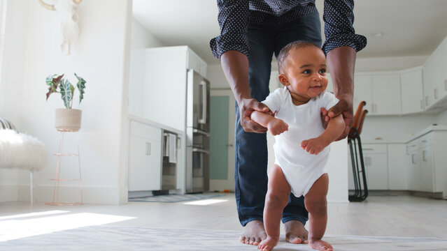 Close Up Of Father Encouraging Smiling Baby Daughter To Take First Steps And Walk At Home