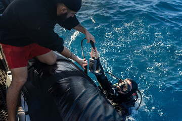 Sailor helping scuba diver getting back on inflatable boat
