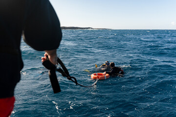 Dive instructor assisting divers at sea with floating safety equipment