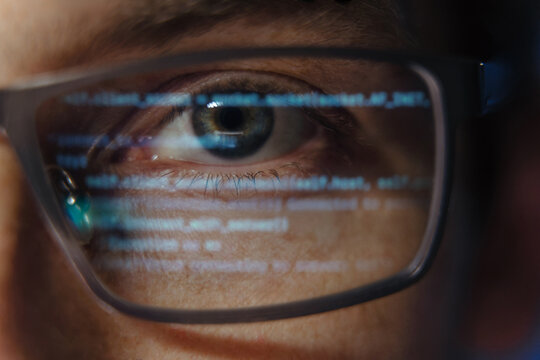 Extreme close-up of a programmer or software engineer eye with computer code reflecting on glasses, symbolizing cybersecurity, coding, and artificial intelligence development. Data science concept