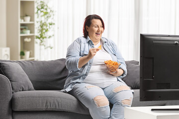 Overweight woman eating crisps and sitting in front of tv