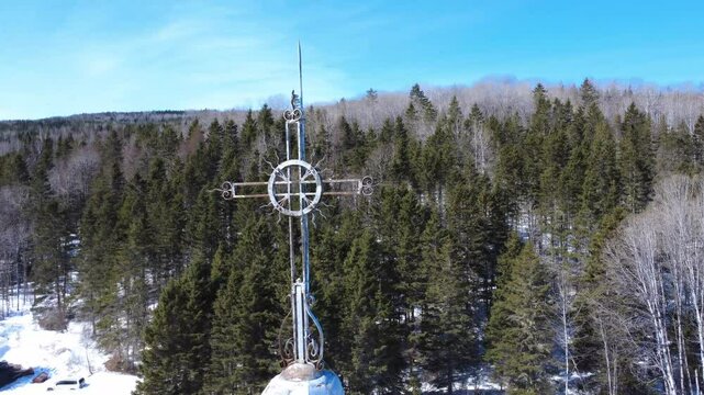 Rotation around a cross atop a church, revealing the rural landscape of the surrounding village with a bridge and a railway. Sainte-Florence, Quebec, Canada, 2025.