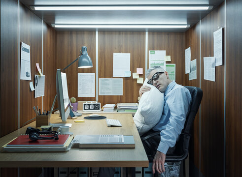 Lazy exhausted employee sleeping at his desk in a tiny office - Powered by Adobe