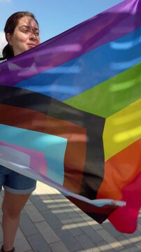 Young woman holding progress pride flag in the wind
