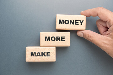 Make More Money concept, closeup hand adding another wood block on the step stairs symbol