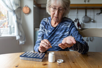 Seated at her kitchen table, an elderly, gray-haired woman meticulously organizes her medicine...