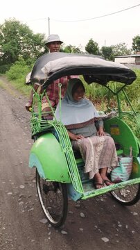 Indonesian driver riding cycle rickshaw with javanese woman in rural road