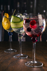 Assorted cocktails with orange, cucumber and berry garnishes served in balloon glasses on a rustic wood surface in a dimly lit bar, ideal for themes like bartending, drinks menu or nightlife.