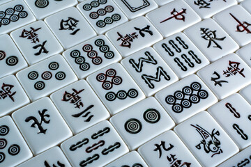 A close-up of a Mahjong tile set, featuring various symbols and characters on white tiles 