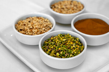 Assorted Ground Nuts and Spices in White Ceramic Bowls – Chopped Pistachios, Hazelnuts, and Cinnamon Powder for Cooking, Baking, Garnishing. High Resolution Food Ingredients Background