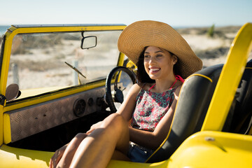 Young adult woman wearing straw hat sitting in dune buggy on coastal dunes, with calm joy